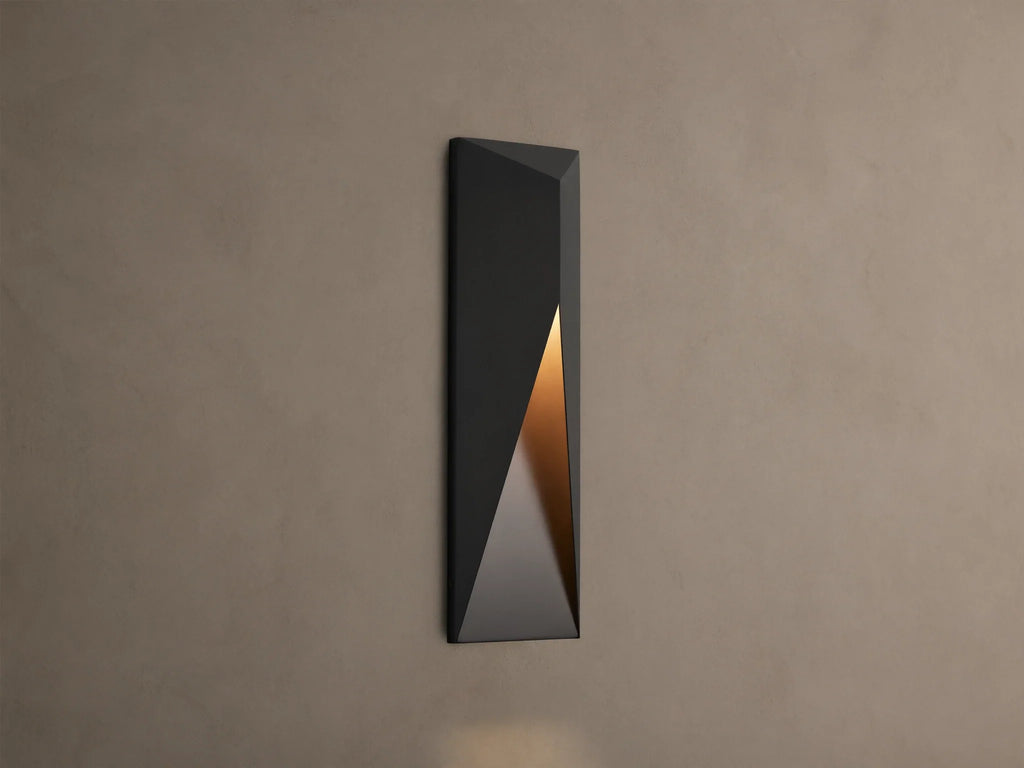 Modern dark grey Davian Outdoor Sconce, vertically mounted, with geometric facets and warm bronze light emanating from inside.