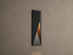 Modern dark grey Davian Outdoor Sconce, vertically mounted, with geometric facets and warm bronze light emanating from inside.