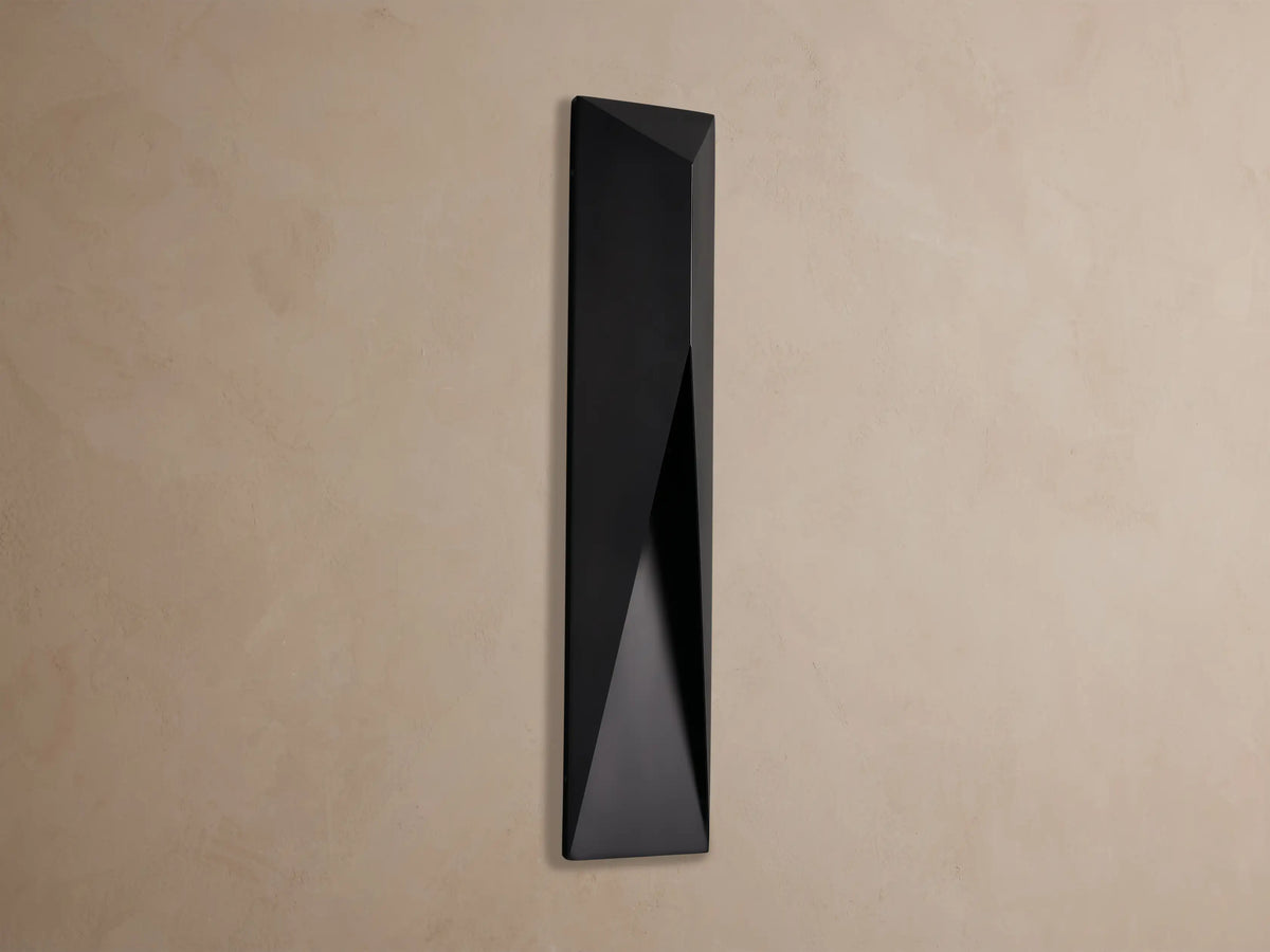 Black, geometric Davian Outdoor Sconce with a bronze interior accent, mounted vertically on a light brown wall.