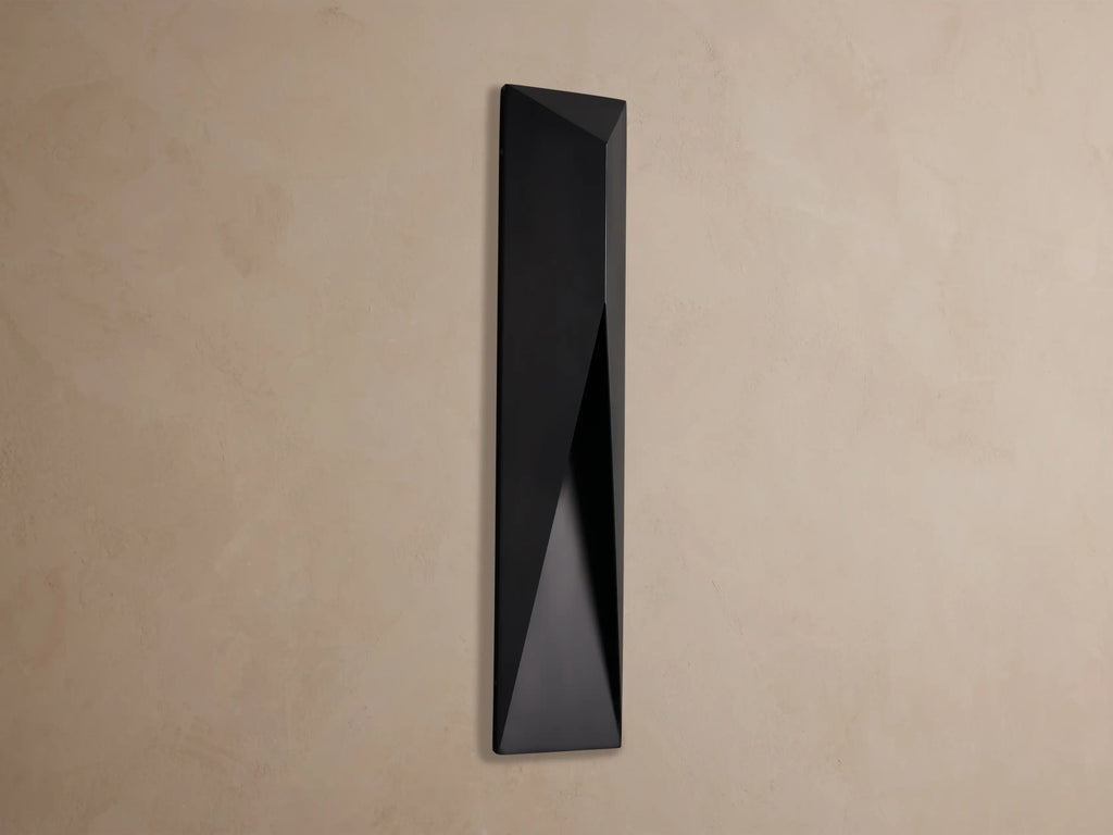 Black, geometric Davian Outdoor Sconce with a bronze interior accent, mounted vertically on a light brown wall.