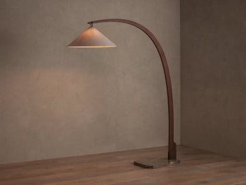 Monviso Floor Lamp with curved walnut wood frame, espresso stone base, and glowing white fabric shade on a wooden floor.