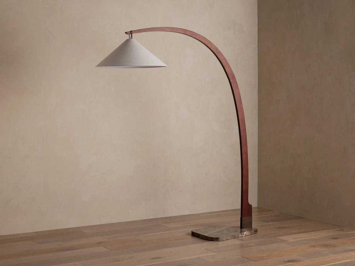 Monviso Floor Lamp with curved walnut wood frame, espresso stone base, and glowing white fabric shade on a wooden floor.
