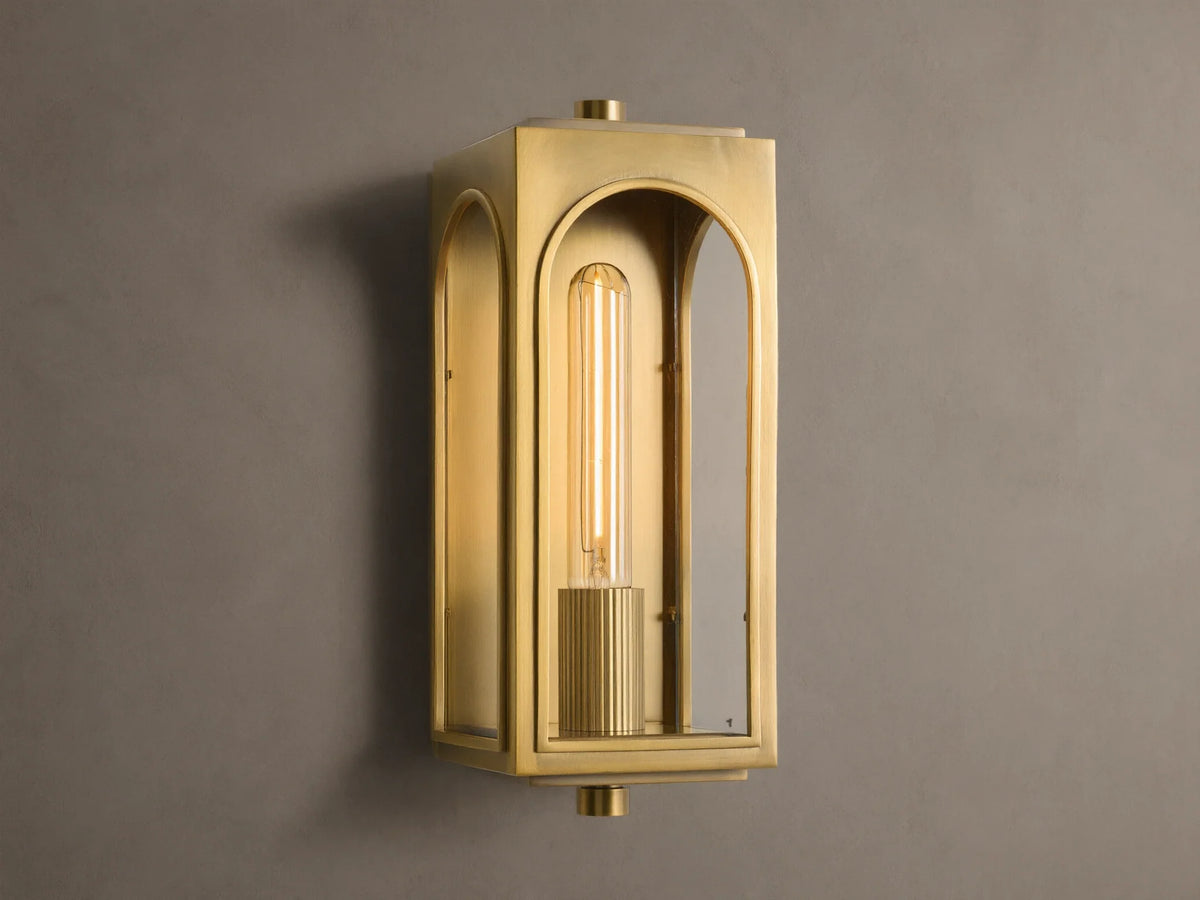 Palladian Outdoor Sconce: Polished brass rectangular fixture with arched glass, bright tubular bulb, mounted on a grey wall.
