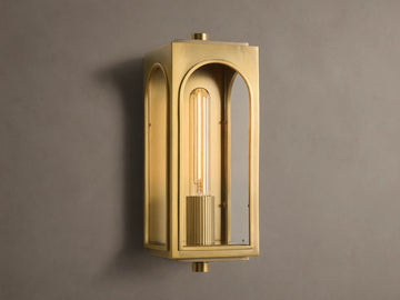 Palladian Outdoor Sconce: Polished brass rectangular fixture with arched glass, bright tubular bulb, mounted on a grey wall.