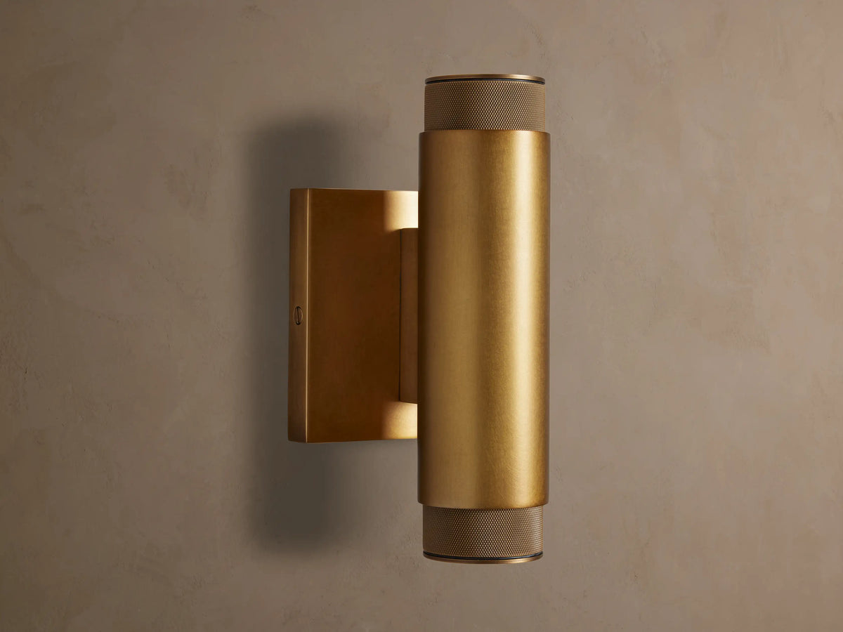 Vertical brass Spotlight Outdoor Sconce, cylindrical, mounted on a wall, with knurled end caps, emitting light up and down.
