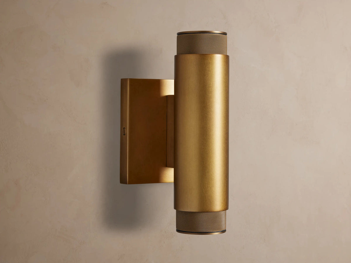 Vertical brass Spotlight Outdoor Sconce, cylindrical, mounted on a wall, with knurled end caps, emitting light up and down.