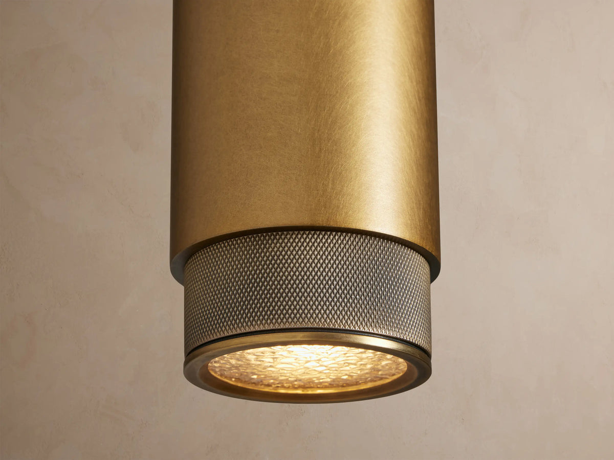 Brass Spotlight Outdoor Sconce, cylindrical and vertical, with dark gray knurled end caps, mounted on a light beige wall.