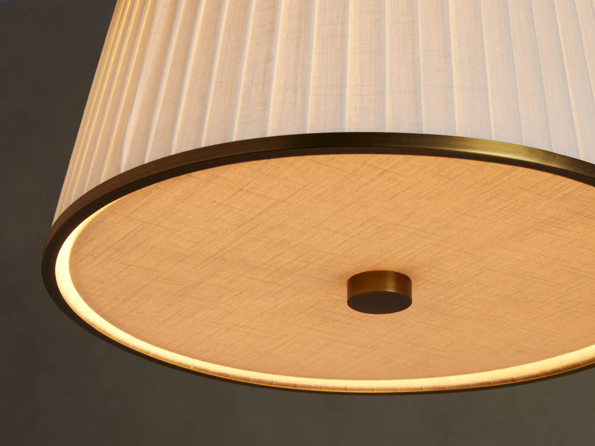 Adria Pendant, a white pleated tapered lampshade with gold metal trim, hanging against a light beige wall.