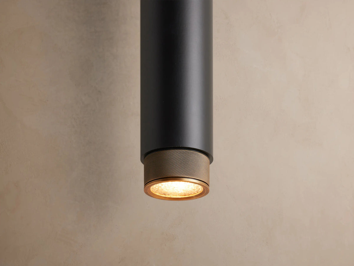 Matte black Spotlight Outdoor Sconce mounted vertically on a light brown wall, featuring brass knurled caps on each end.