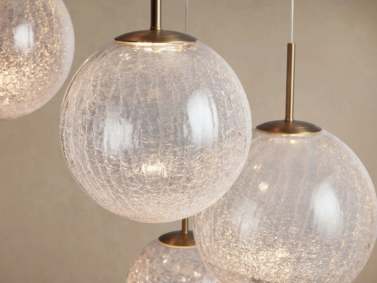 Casen Round Chandelier featuring multiple illuminated crackle glass globes suspended by satin brass rods against a light wall.
