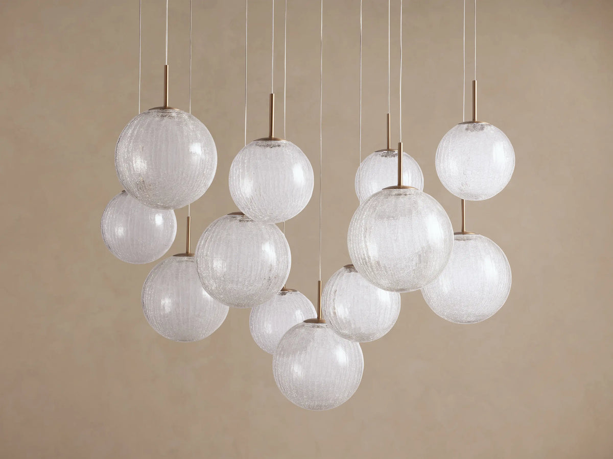 Casen Round Chandelier: multiple clear crackle glass globes hang from satin brass rods & thin wires against a light beige wall.