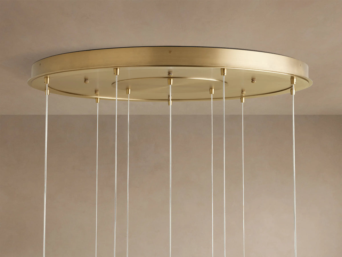 Casen Round Chandelier with a round satin brass canopy mounted on a light-colored ceiling, multiple clear cables hang down.