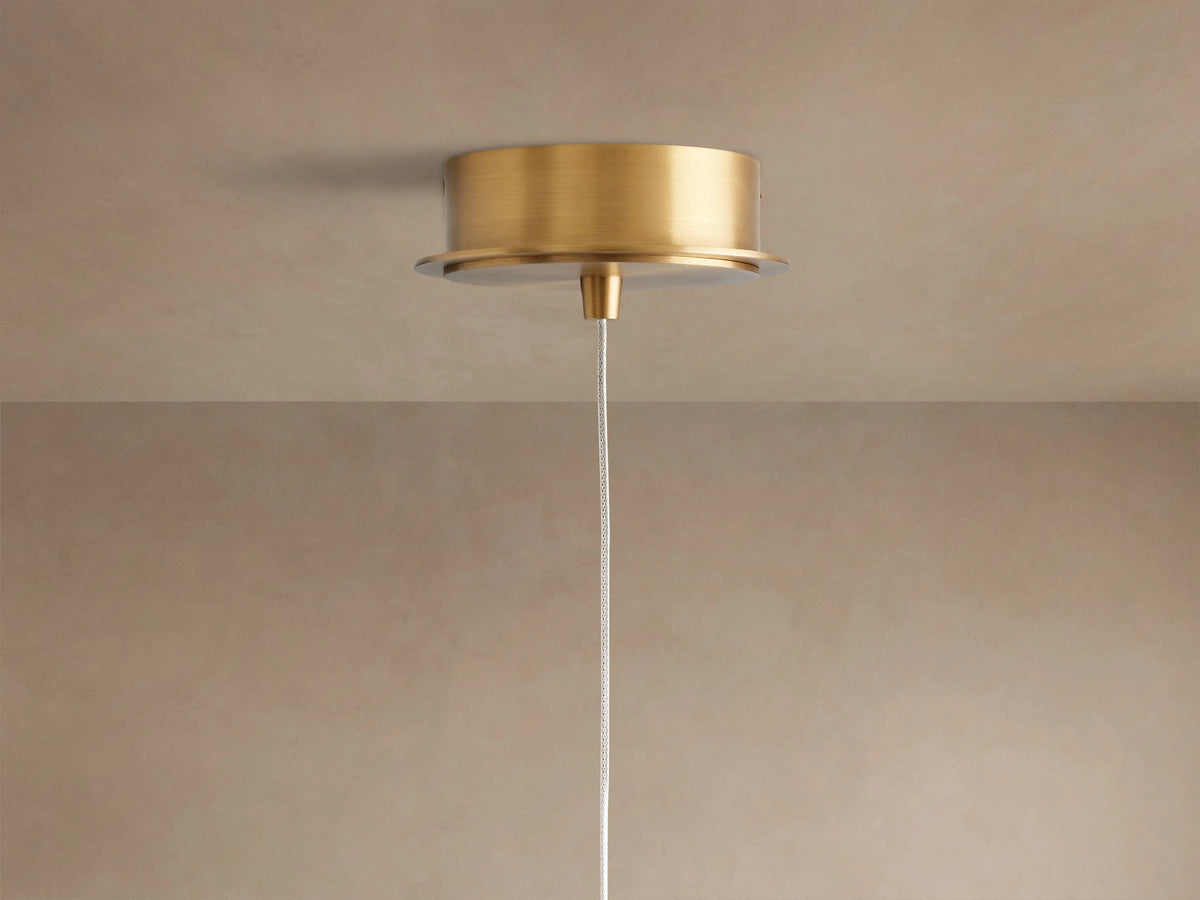 Close-up of Casen Pendant. Illuminated crackle glass globe with warm light, connected to a brushed brass rod.