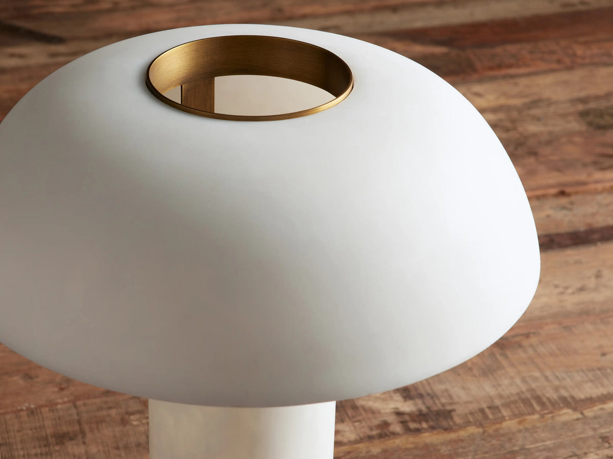 Tramonto Table Lamp with a white cloudstone resin cylindrical base, a white dome shade, and brass accents on a wood table.