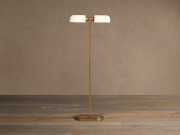 Zayd Floor Lamp: elegant brass with two illuminated oblong opal glass shades and an oval base, standing on a wooden floor.