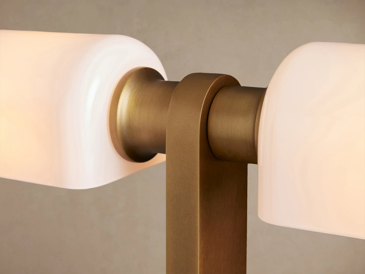 Zayd Floor Lamp, brass-finished with two rectangular white opal glass shades, standing upright on a wooden floor against a beige wall.