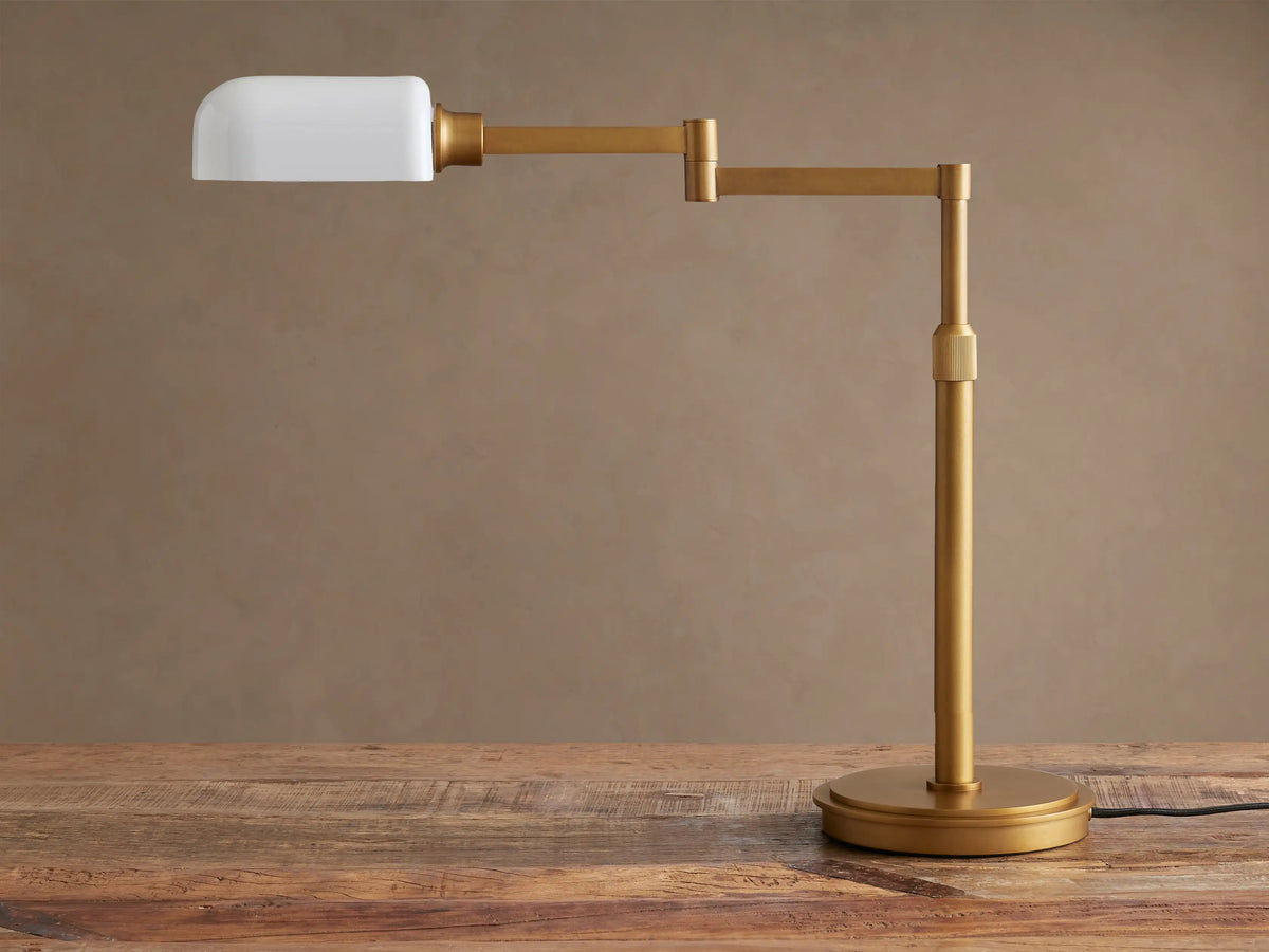 Brass Zayd Swing Arm Table Lamp with white opal glass shade, adjustable arm extended, on a wooden table.
