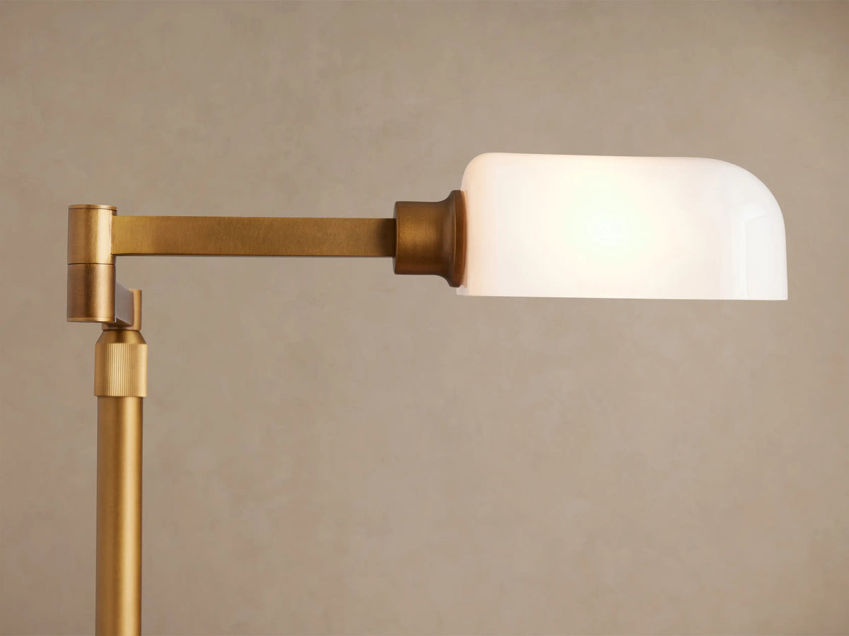 Zayd Swing Arm Table Lamp with illuminated white opal glass shade and articulated golden brass arm against a light wall.