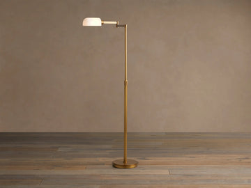 Zayd Swing Arm Floor Lamp, brass with an extended arm, illuminated opal glass shade, on a wooden floor.