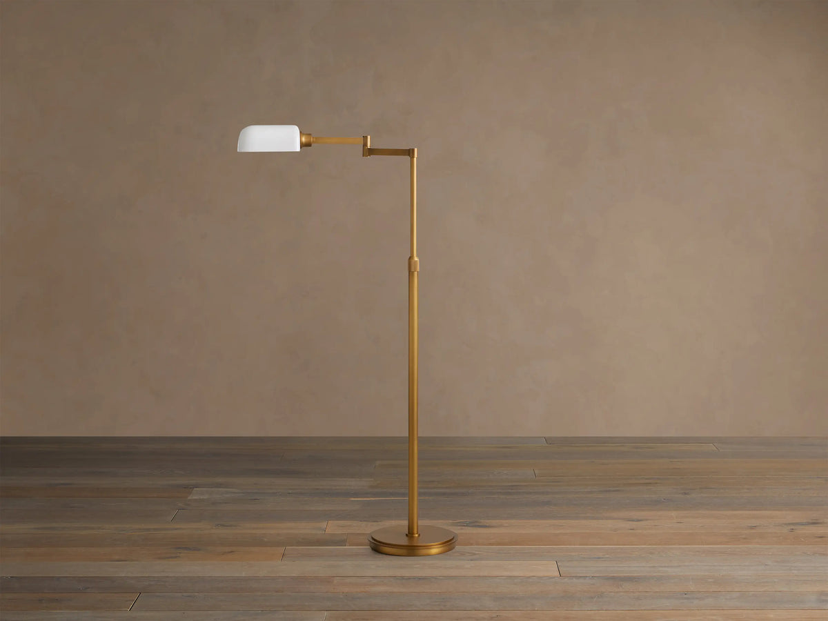 Zayd Swing Arm Floor Lamp, brass with an extended arm, illuminated opal glass shade, on a wooden floor.