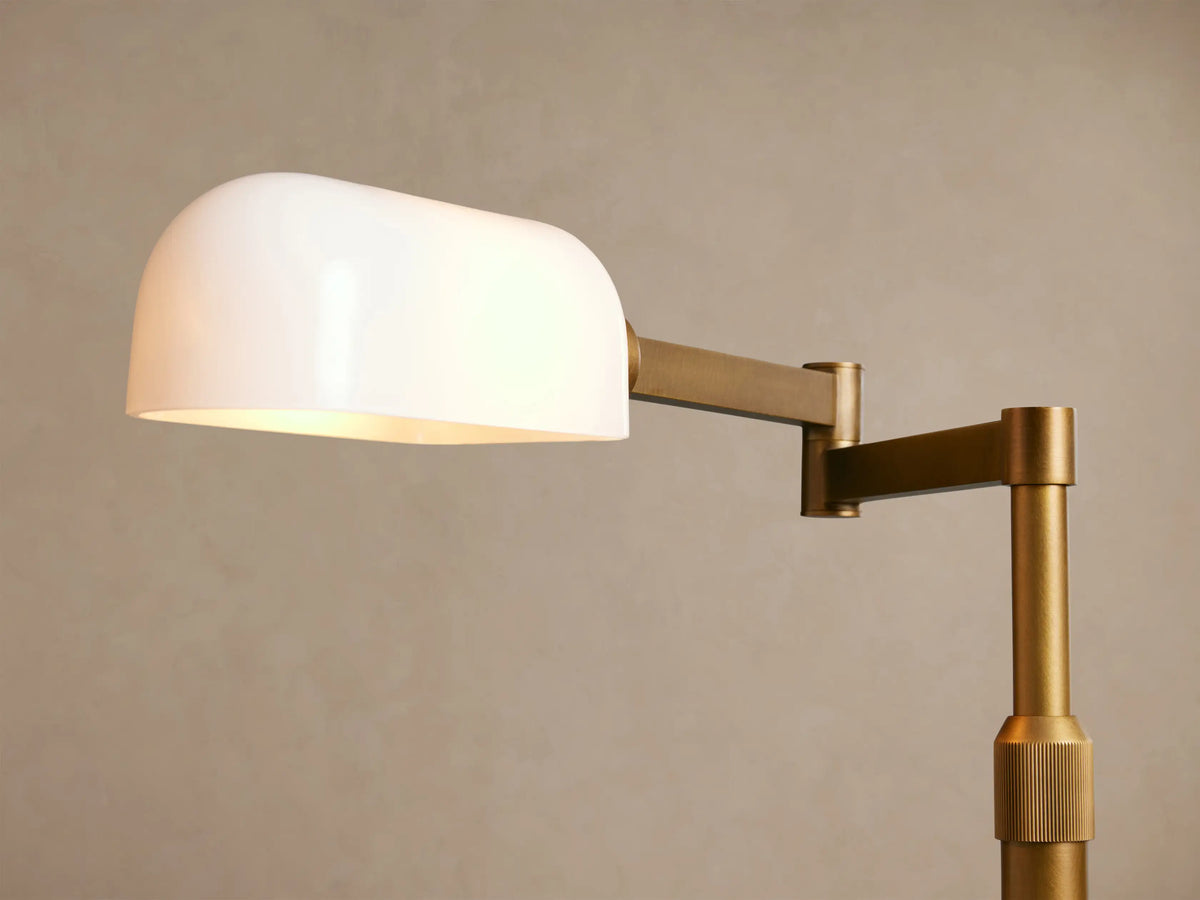 Tall brass Zayd Swing Arm Floor Lamp with a round base, L-shaped arm, and rectangular white opal glass shade, on a wooden floor.