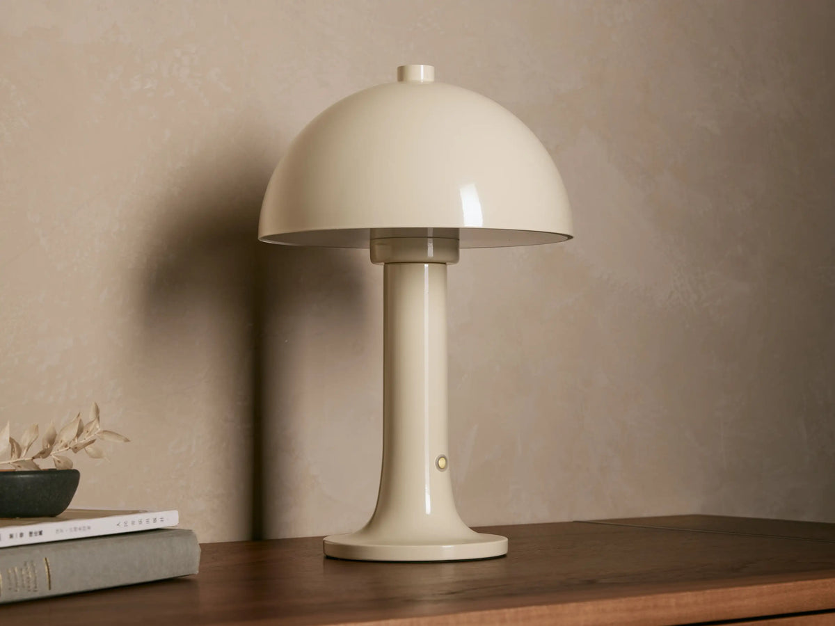 Cream Jocy Portable Table Lamp with mushroom-style dome shade, emitting warm light on a wooden table with books.