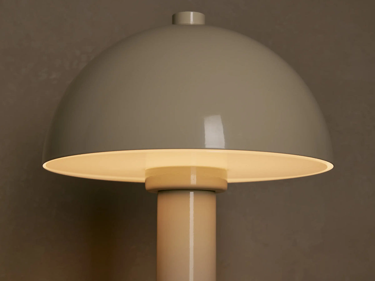 Cream Jocy Portable Table Lamp with a dome shade and cylindrical base on a wooden surface against a light wall. Gold touch control.