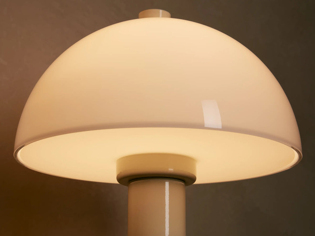 Jocy Portable Table Lamp with cream lacquered base and white opal dome shade, on a wooden table next to a book.