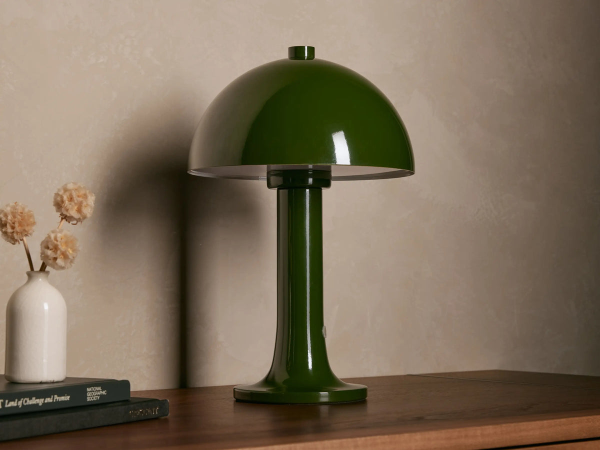 Jocy Portable Table Lamp, dark green lacquered metal, mushroom-shaped, illuminated on a wooden table. Books & vase nearby.