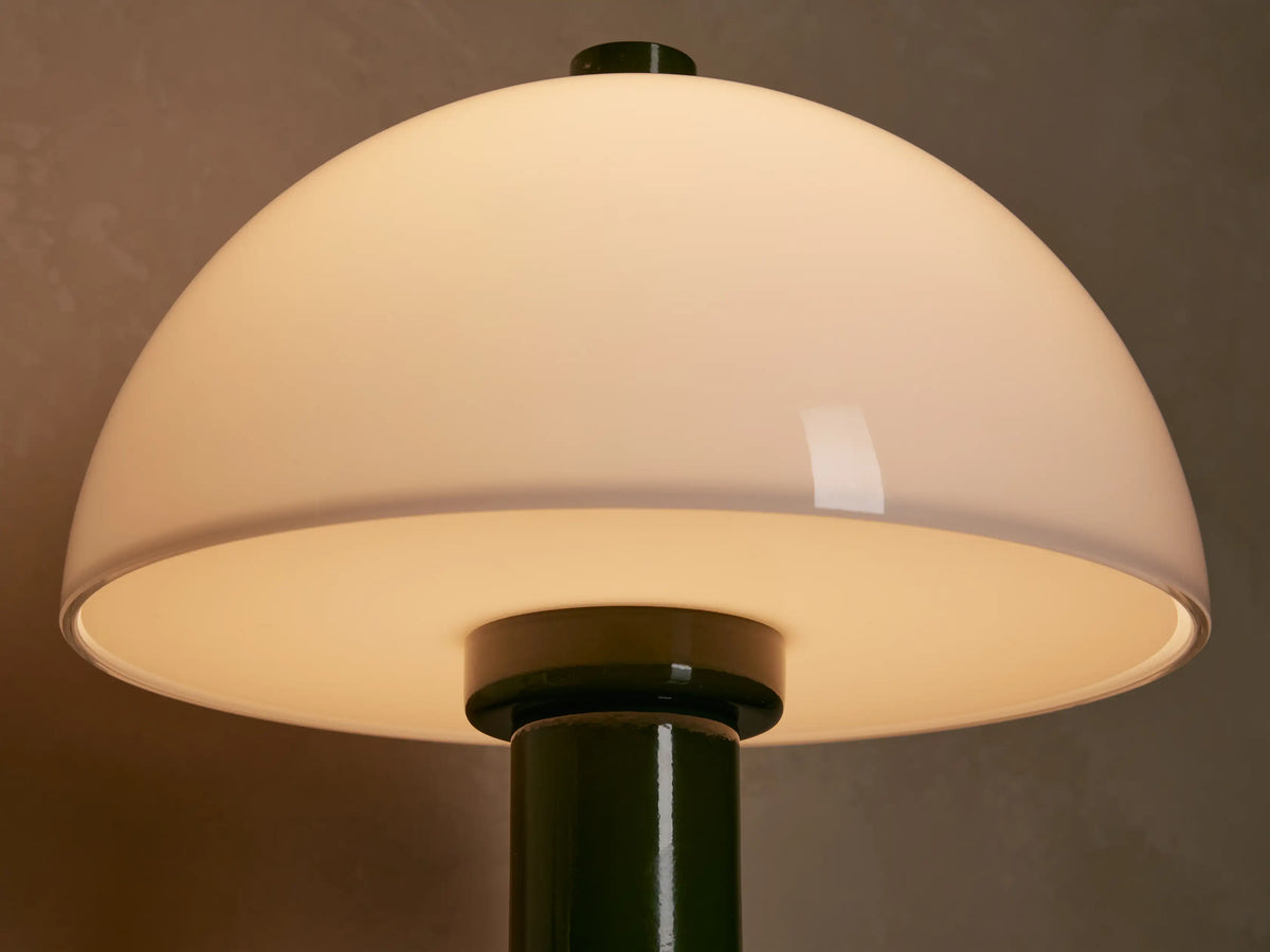 Jocy Portable Table Lamp with green base and white dome shade, on a wooden table next to books.