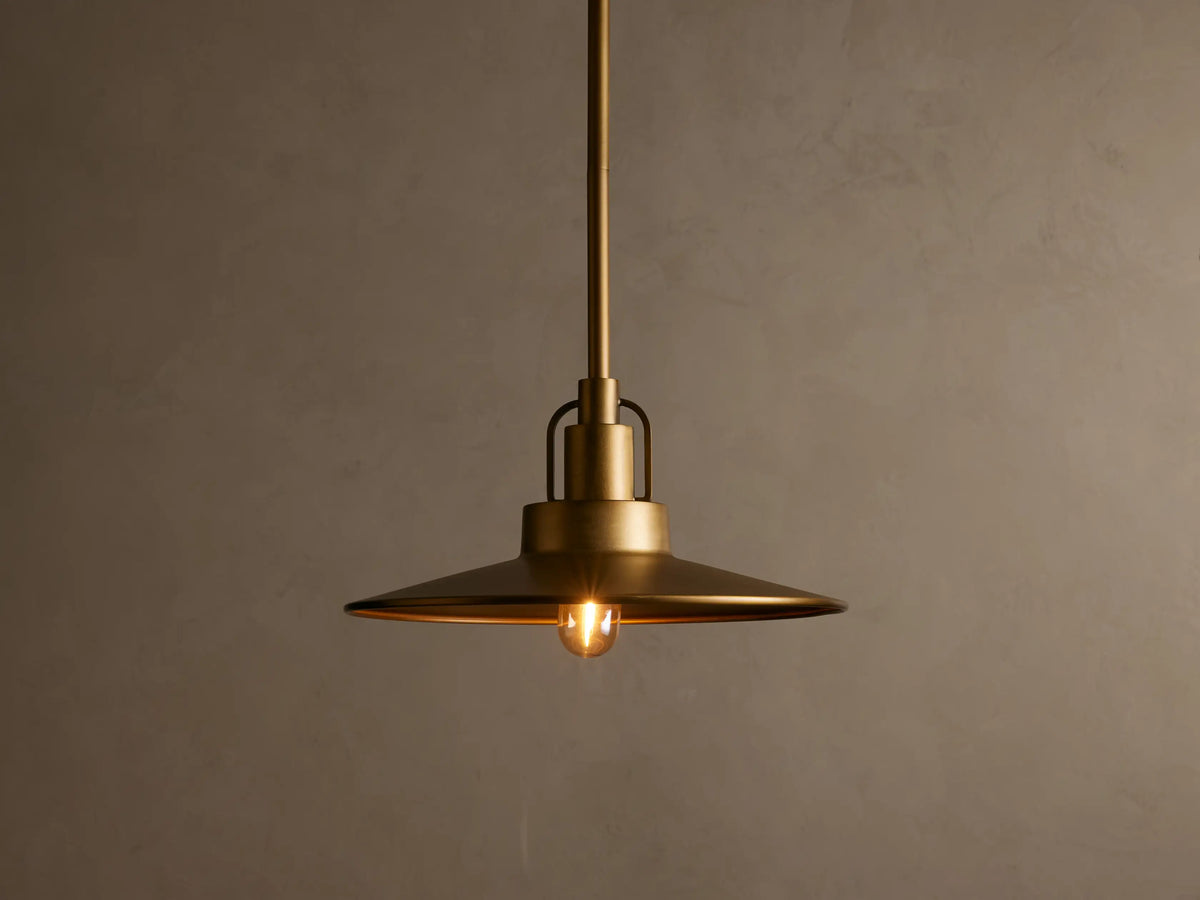 A bronze pendant light with a dome-shaped amber glass shade, emitting a warm glow against a neutral background.