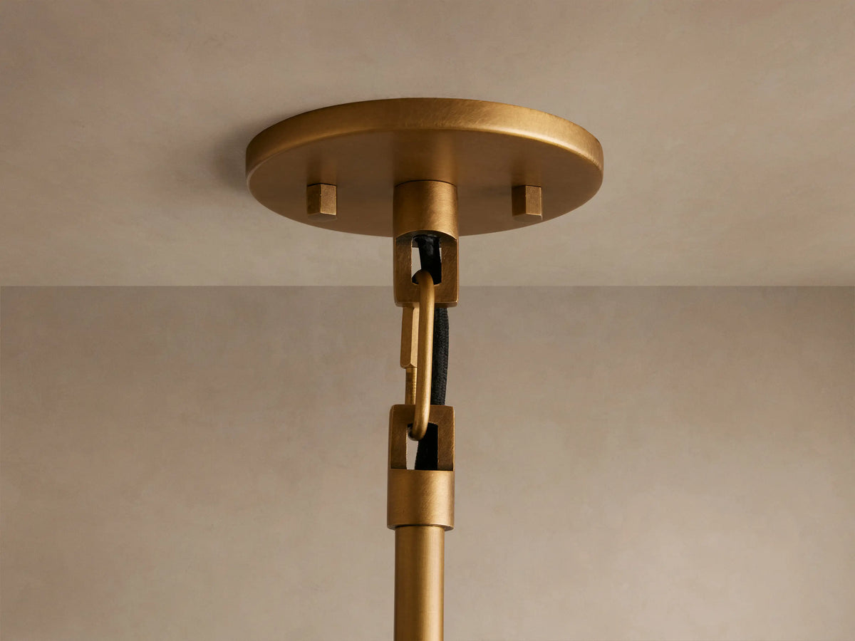 A brass pendant light with a wide, flat shade hangs from the ceiling. The light bulb glows warmly beneath the metallic shade.
