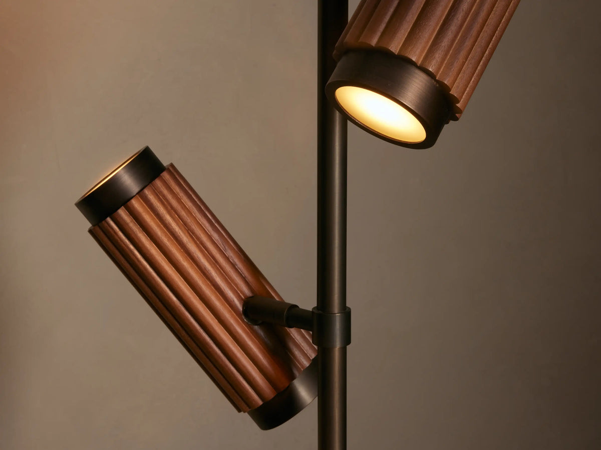 Decan Task Floor Lamp, dark bronze metal with two angled fluted walnut wood lamp heads, on a wood floor against a light wall.