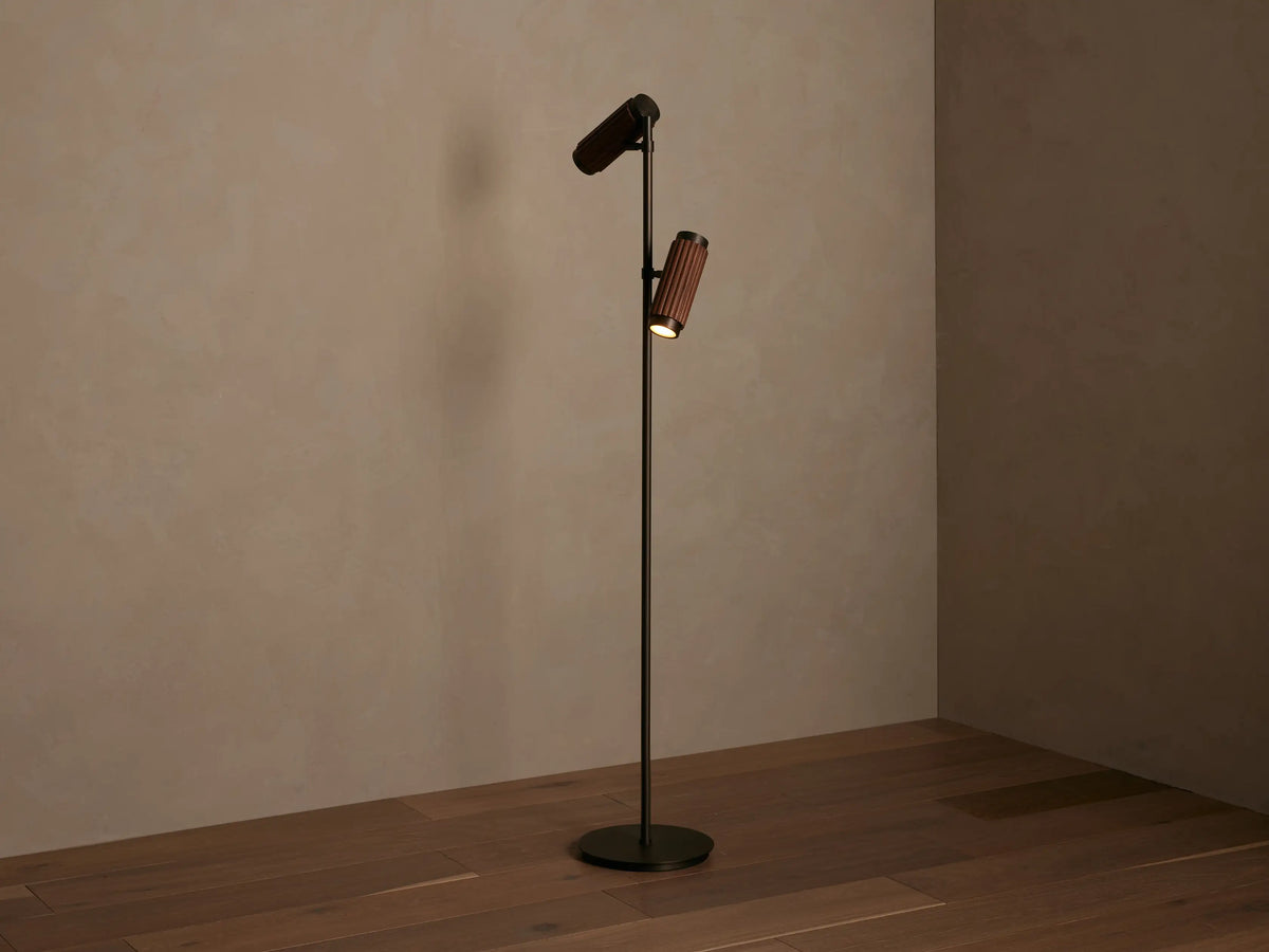Decan Task Floor Lamp with two angled light heads featuring fluted walnut wood and bronze accents. One light is illuminated.