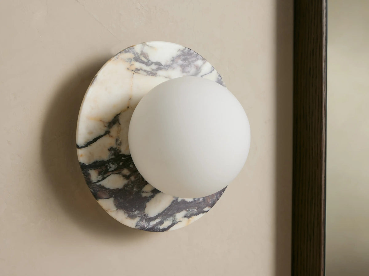 Corinna Sconce: Wall-mounted circular marble base with black and cream veining, holding a glowing, milky white glass globe.