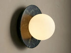 Corinna Sconce: Round dark green marble backplate with white veins, supporting a spherical milk glass globe on a beige wall.