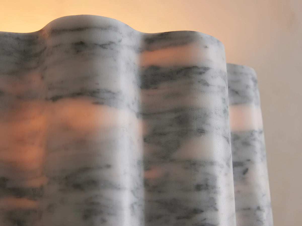A wavy, marble-textured lamp with gray and white patterns, illuminated from inside, casting a warm glow, against a light background.