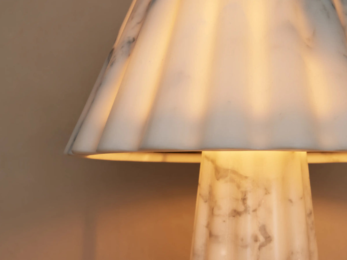 Marble table lamp with a fluted base and shade, featuring a white and gray veined pattern, placed on a wooden surface.