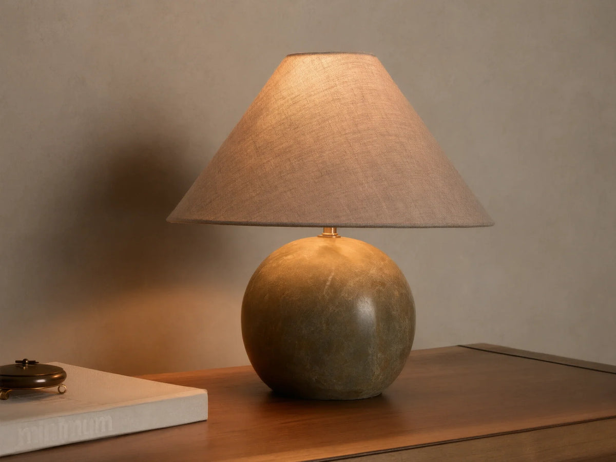 Front view of a table lamp with a round, mottled dark green stone base and an illuminated light brown conical fabric shade.