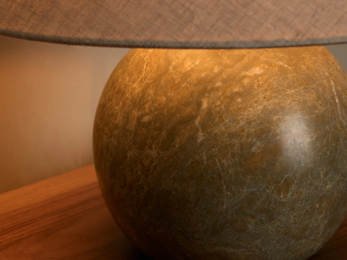 Close-up of a lit lamp featuring a round, earthy green-brown marbled base and a grey fabric lampshade.
