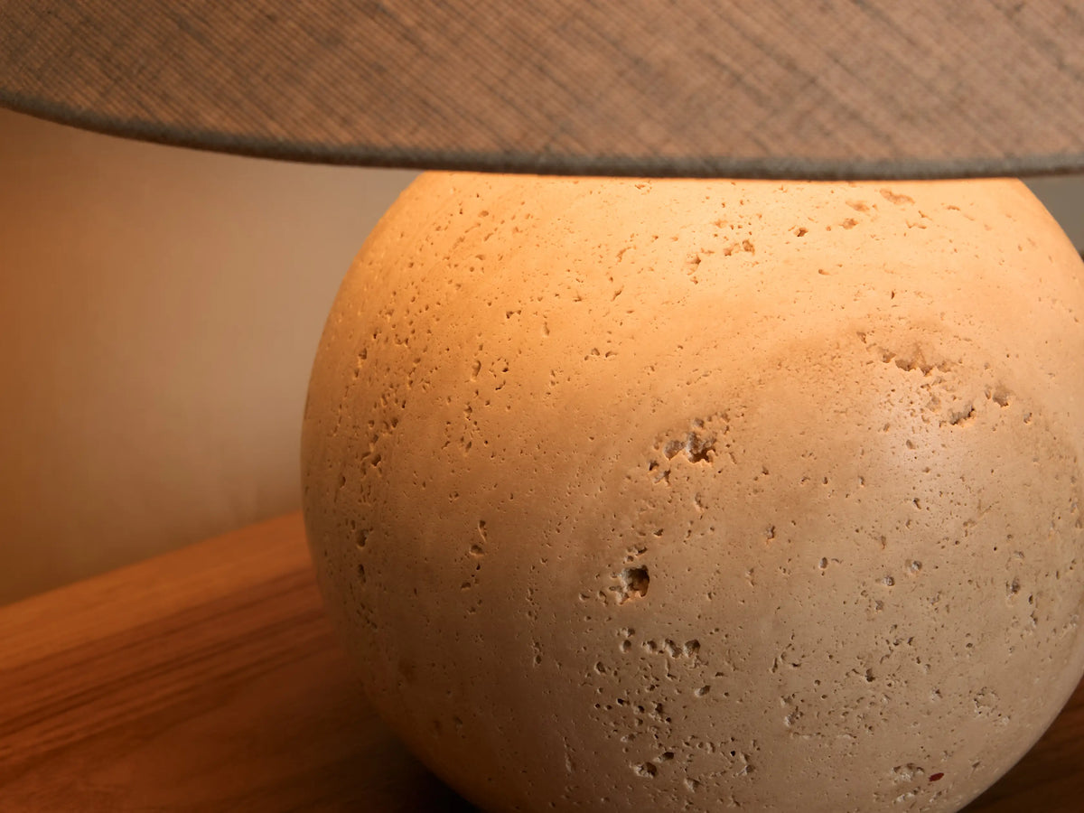 Close-up of a spherical light beige porous stone lamp base with a dark gray fabric shade, casting a warm glow.