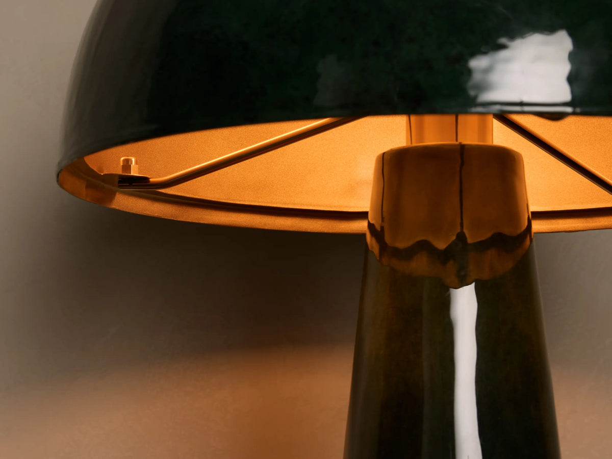 Close-up of a glossy dark green bell-shaped lamp shade with a glowing orange interior and textured dark green base.