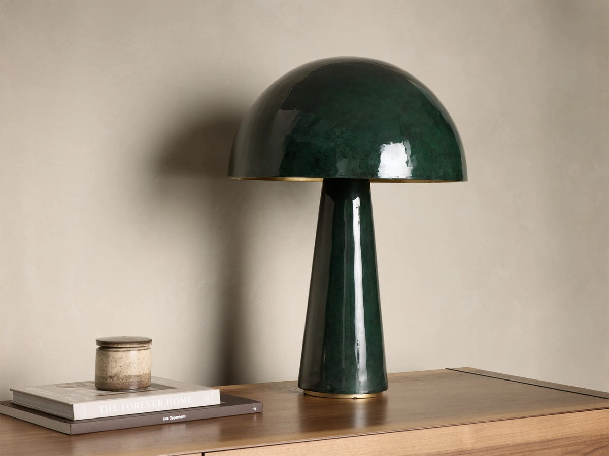 Glossy dark green mushroom-shaped table lamp with a gold base accent, placed on a wooden nightstand with books.