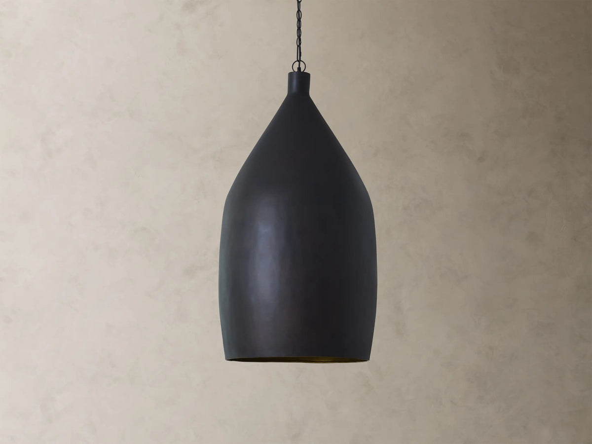 A matte black, bell-shaped pendant light hangs against a textured beige wall, casting a warm glow from its interior.
