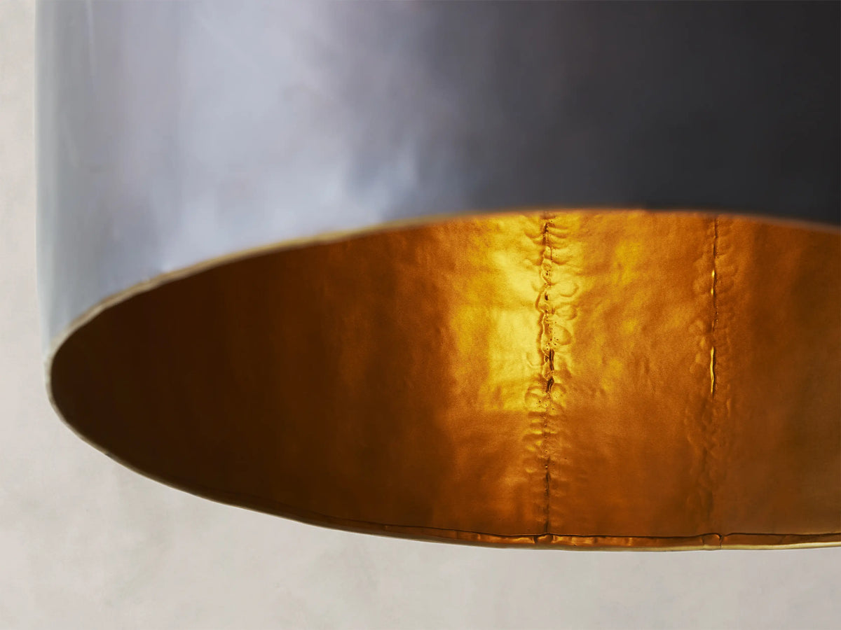 A sleek black pendant light with a conical shape hangs from a chain against a beige textured wall.