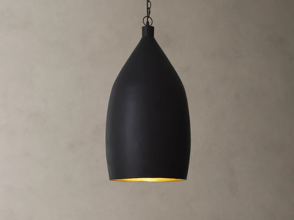 A matte black pendant light with a smooth, teardrop shape hanging from a chain against a beige textured wall.