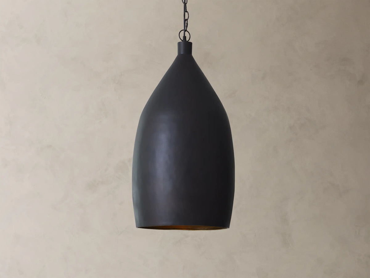 A matte black pendant light with a smooth, teardrop shape hanging from a chain against a beige textured wall.