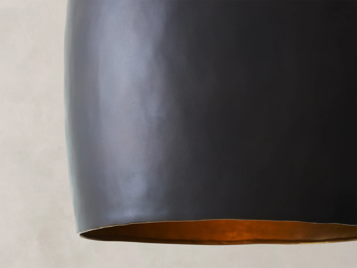 Black, cone-shaped pendant light with a smooth matte finish hanging from a chain against a textured beige wall.