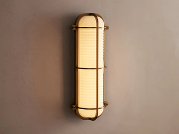 Solomon Outdoor Sconce, vertical, brass-framed, with glowing ribbed milk glass diffuser mounted on a neutral-colored wall.