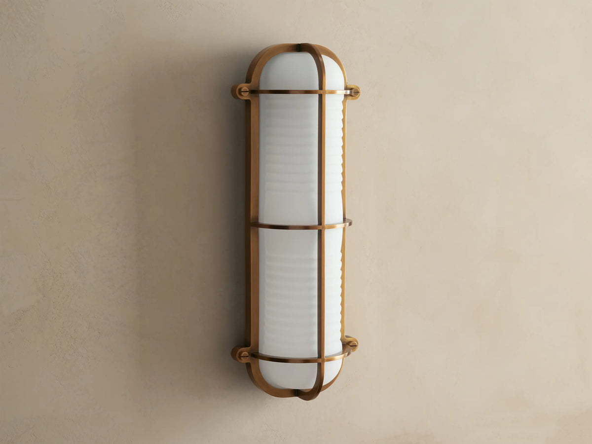Solomon Outdoor Sconce, vertical, brass-framed, with glowing ribbed milk glass diffuser mounted on a neutral-colored wall.